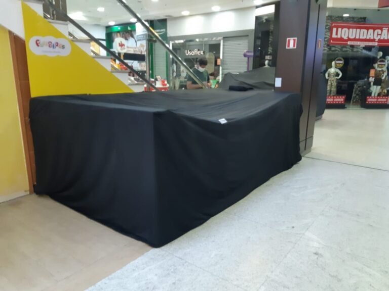Fechamento diário com capa preta para quiosque de canto, posicionado próximo à escada rolante do shopping. Segurança para o estoque e adequação às regras do centro comercial.